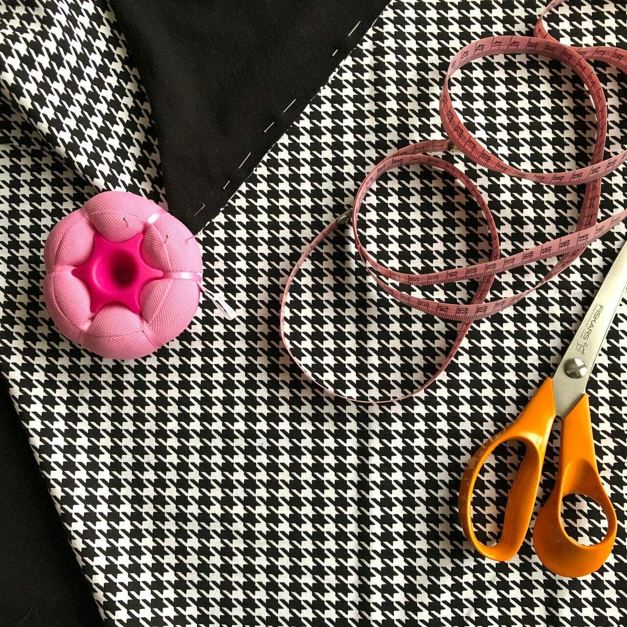 Scissors, measuring tape, and pin cushion on houndstooth fabric — workroom essentials